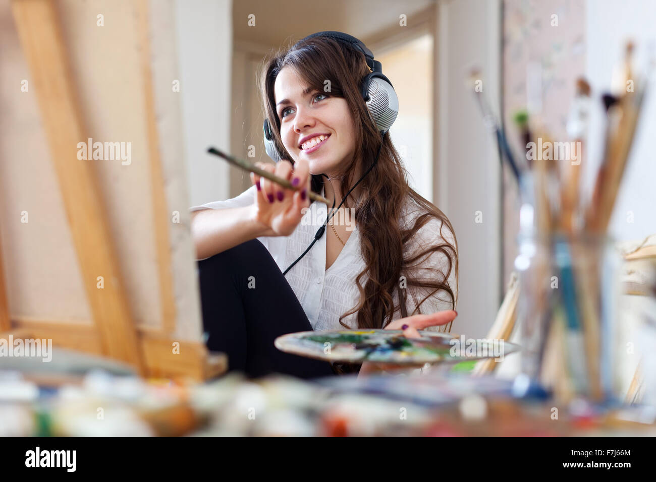Long-haired female artist in headphones paints picture on canvas with ...