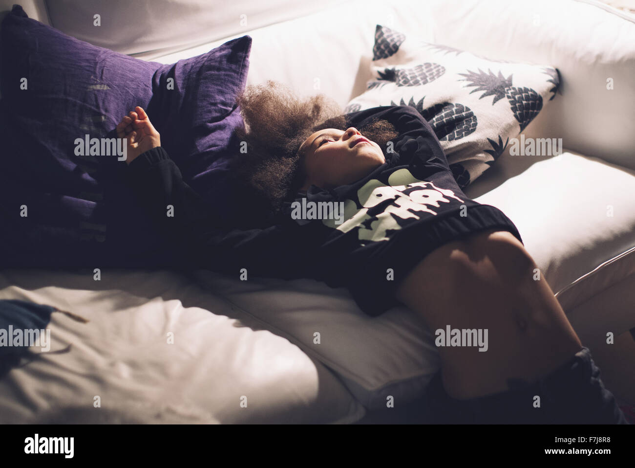 Girl leaning back against sofa, daydreaming Stock Photo