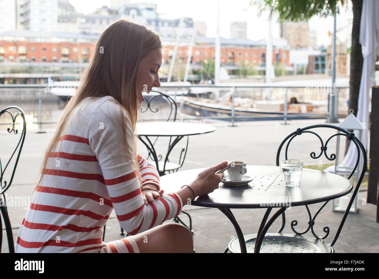 Young woman sitting at sidewalk cafe, laughing at smartphone Stock Photo