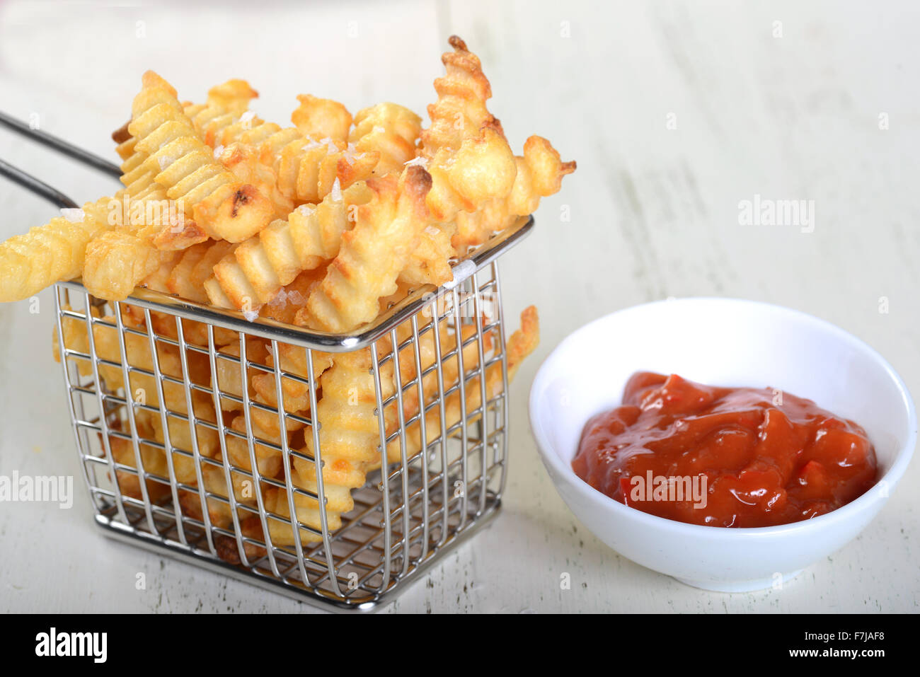 Crispy French Fries in a wire fryer basket with a spicy red pepper aoli Stock Photo