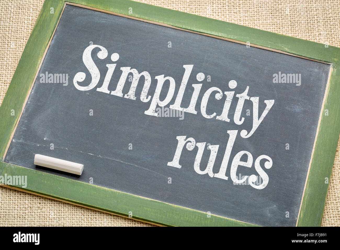 simplicity rules sign - white chalk text on a vintage slate blackboard  against burlap canvas Stock Photo