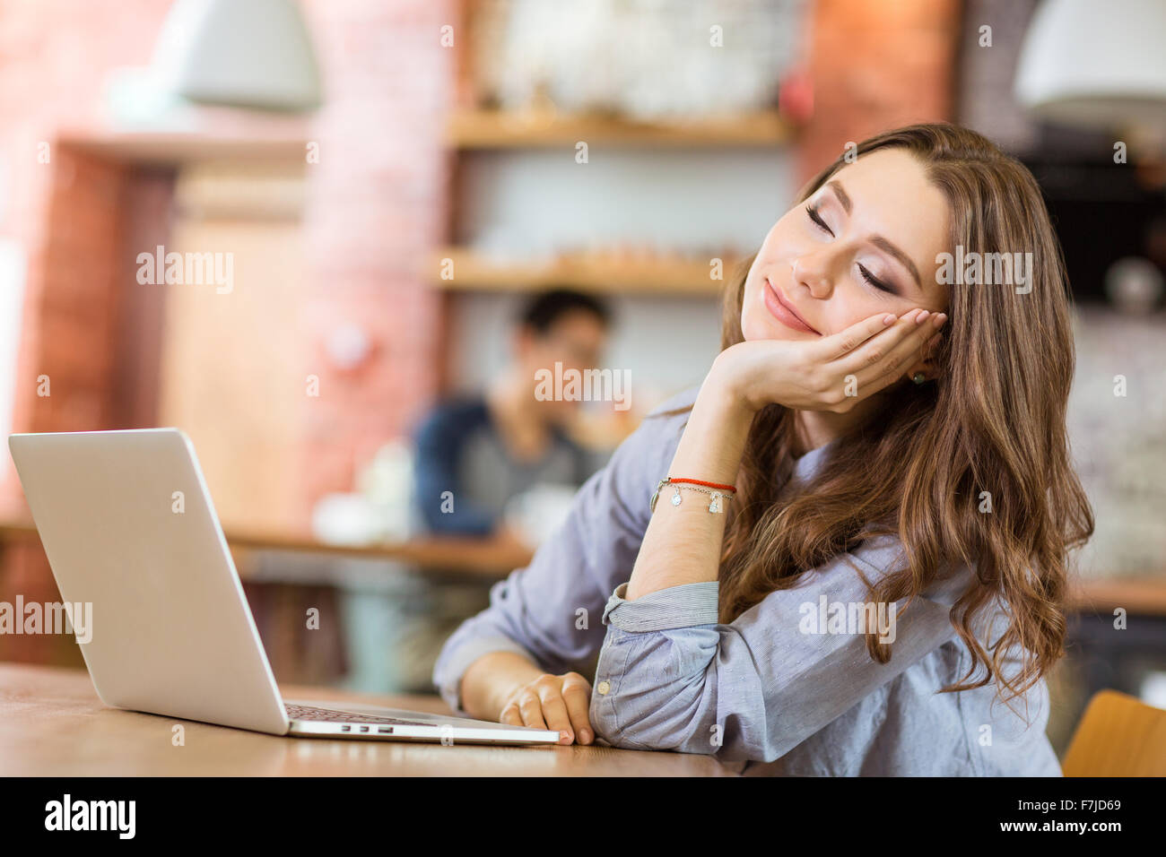 Attractive relaxed curly young woman sitting in cafe with closed eyes, smiling and dreaming Stock Photo