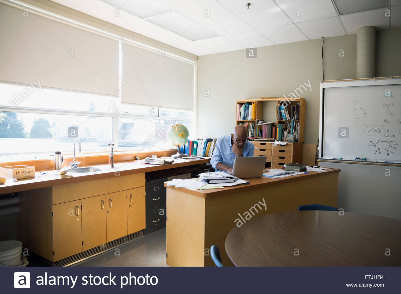 Teacher working at laptop in classroom Stock Photo