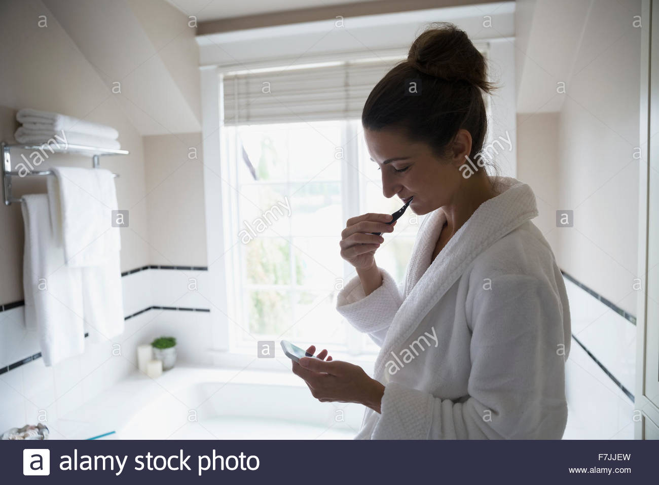 Woman texting and brushing teeth in bathroom Stock Photo