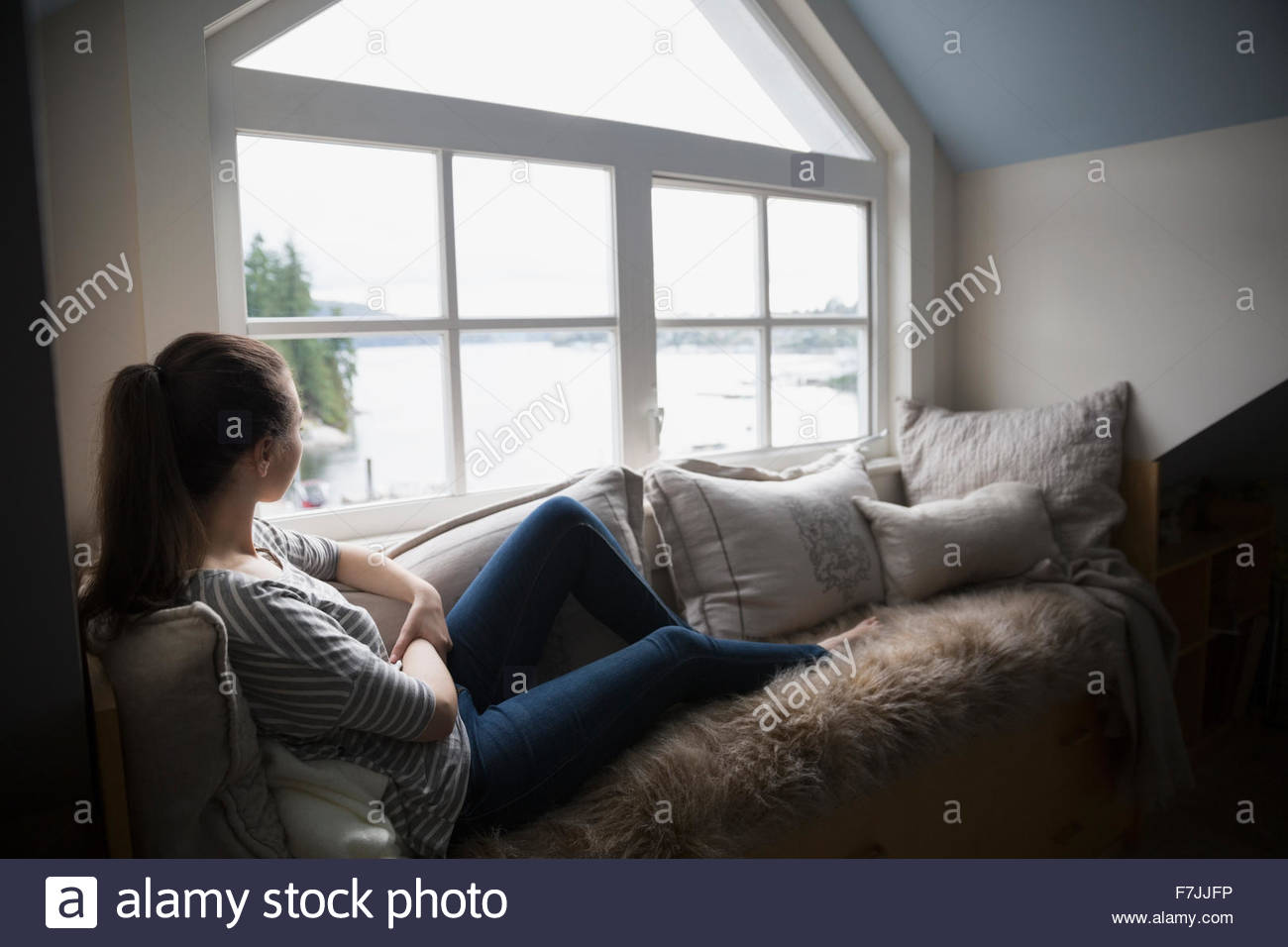 Pensive young woman looking out window lake view Stock Photo