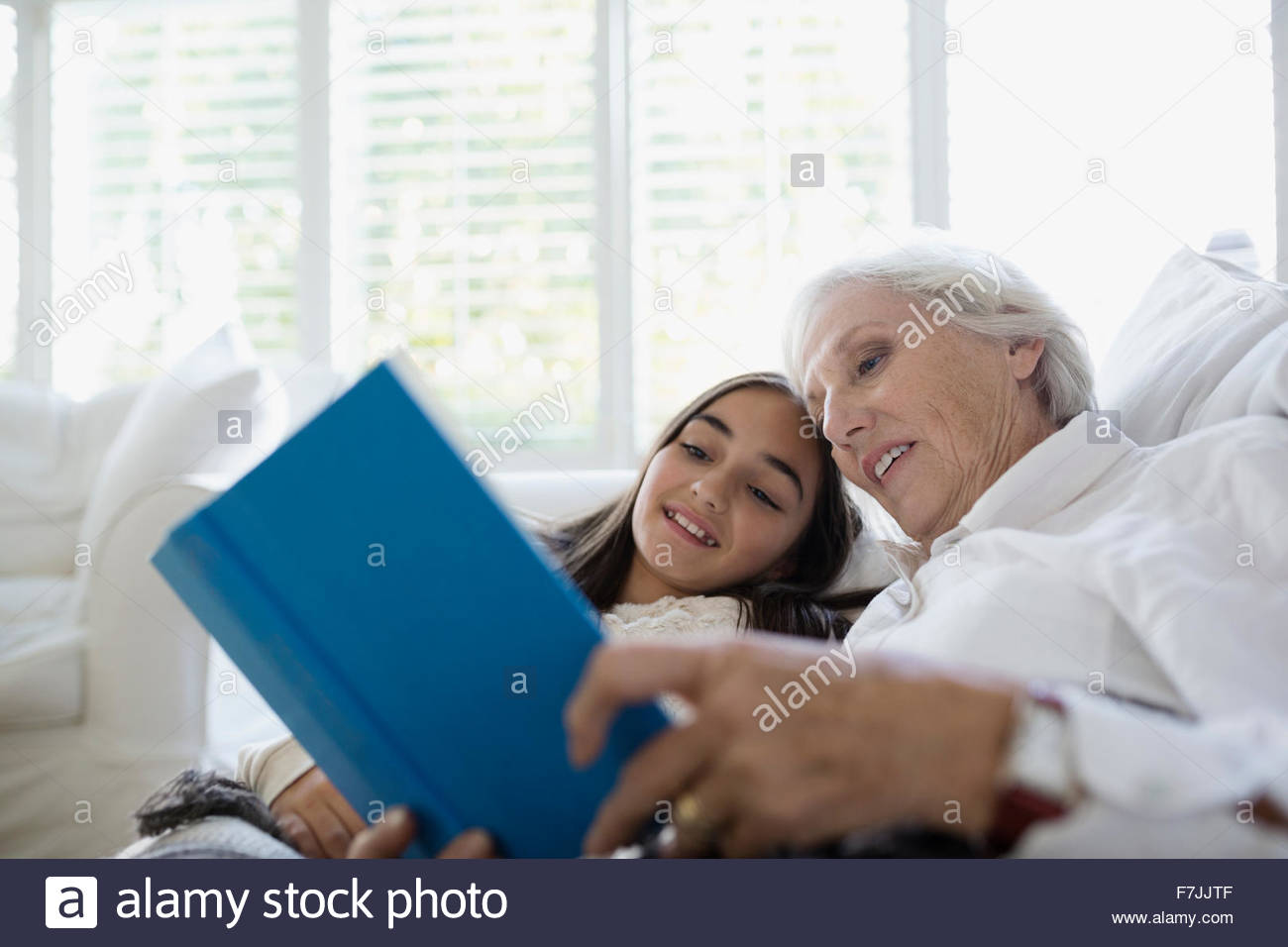 Grandmother and granddaughter reading book on sofa Stock Photo