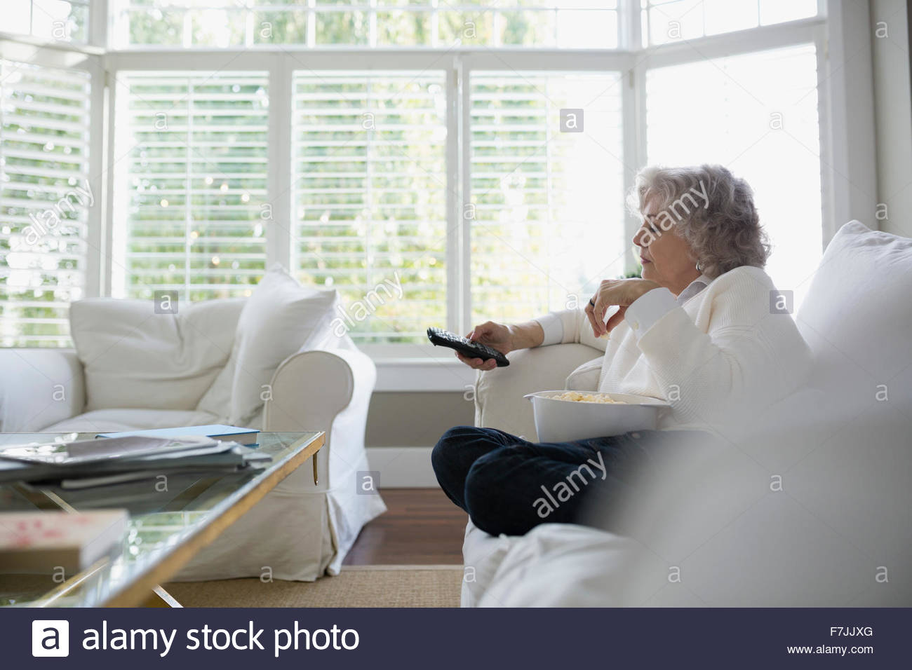 Senior woman watching TV with popcorn on sofa Stock Photo