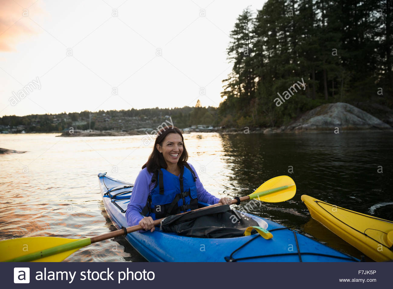 Smiling woman kayaking on lake at sunset Stock Photo