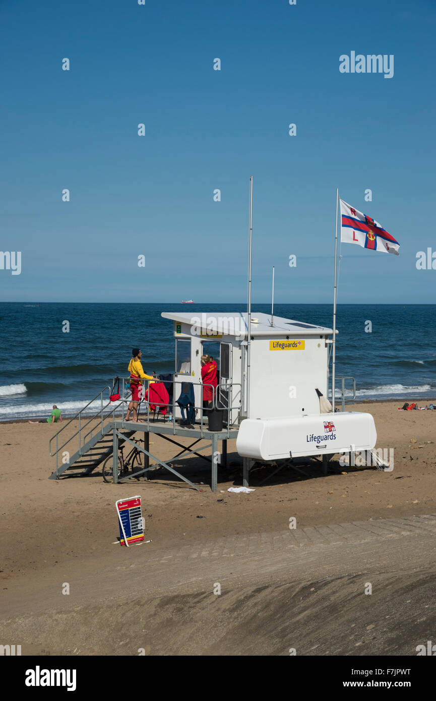 Summer sun, blue sky & sea, Sandsend, Yorkshire Coast, England, UK - shoreline is quiet, RNLI flag is flying & lifeguards are patrolling the beach. Stock Photo