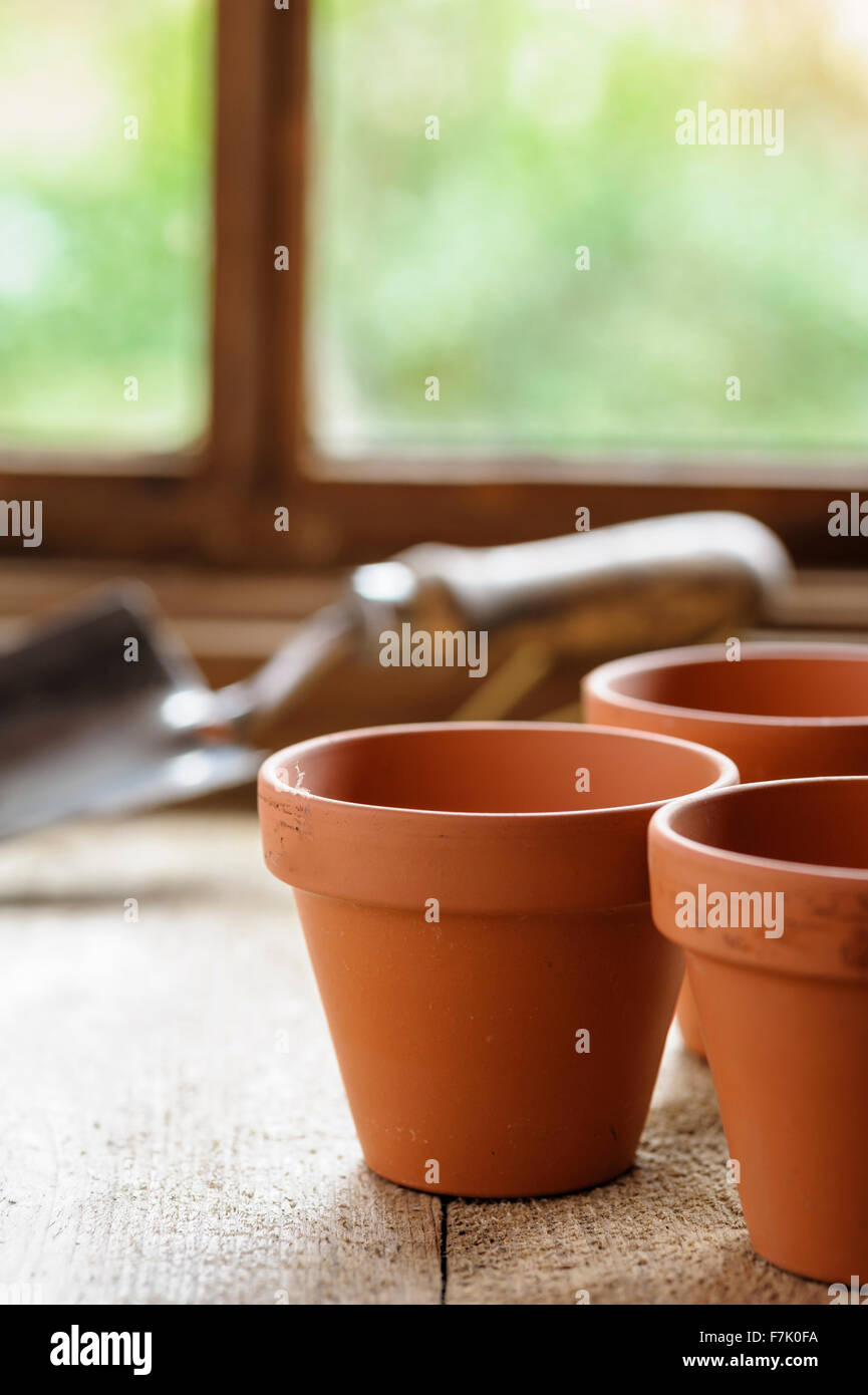 Three terracotta pots on a potting bench, with hand trowel in background. Stock Photo