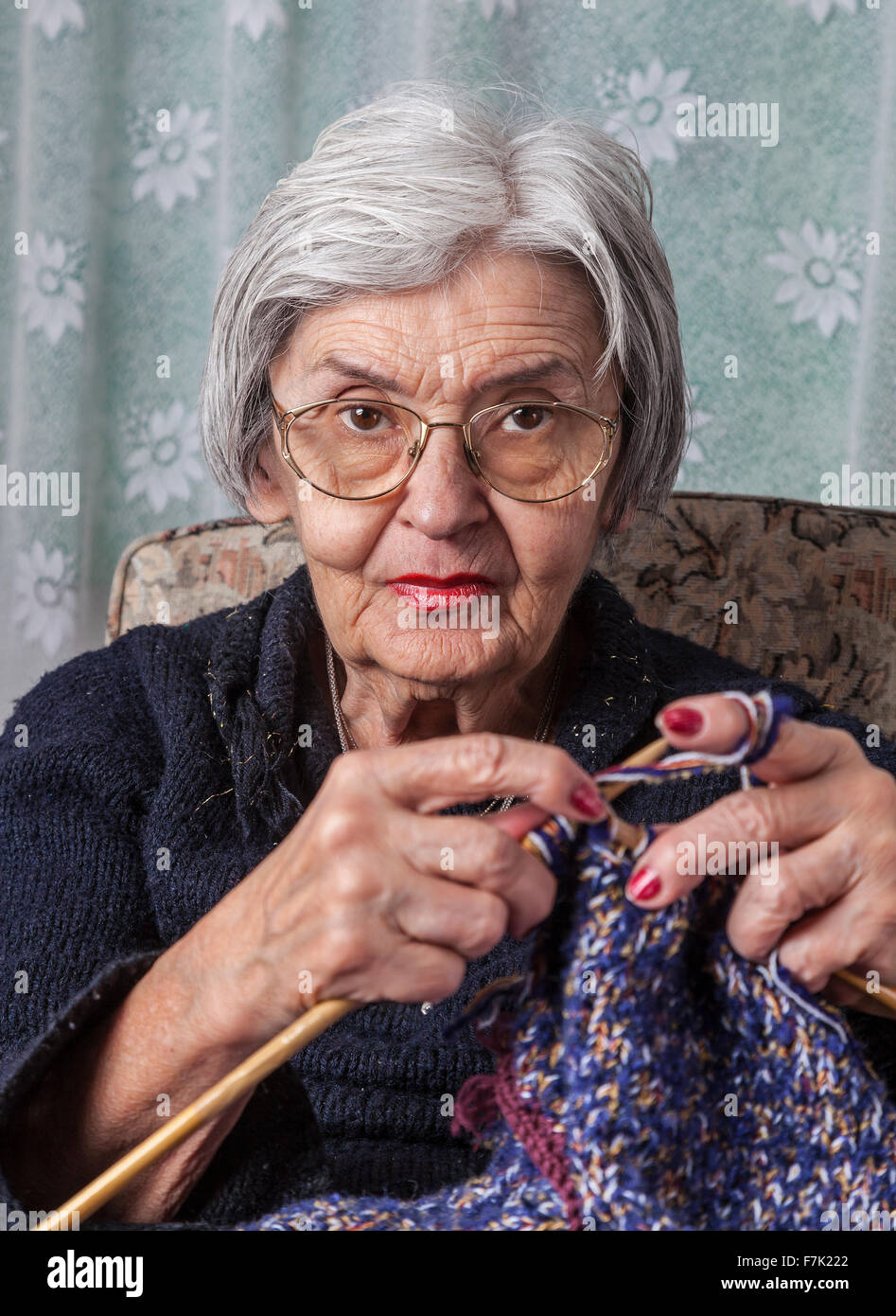 Portrait of an old wrinkled woman knitting in her home. Stock Photo