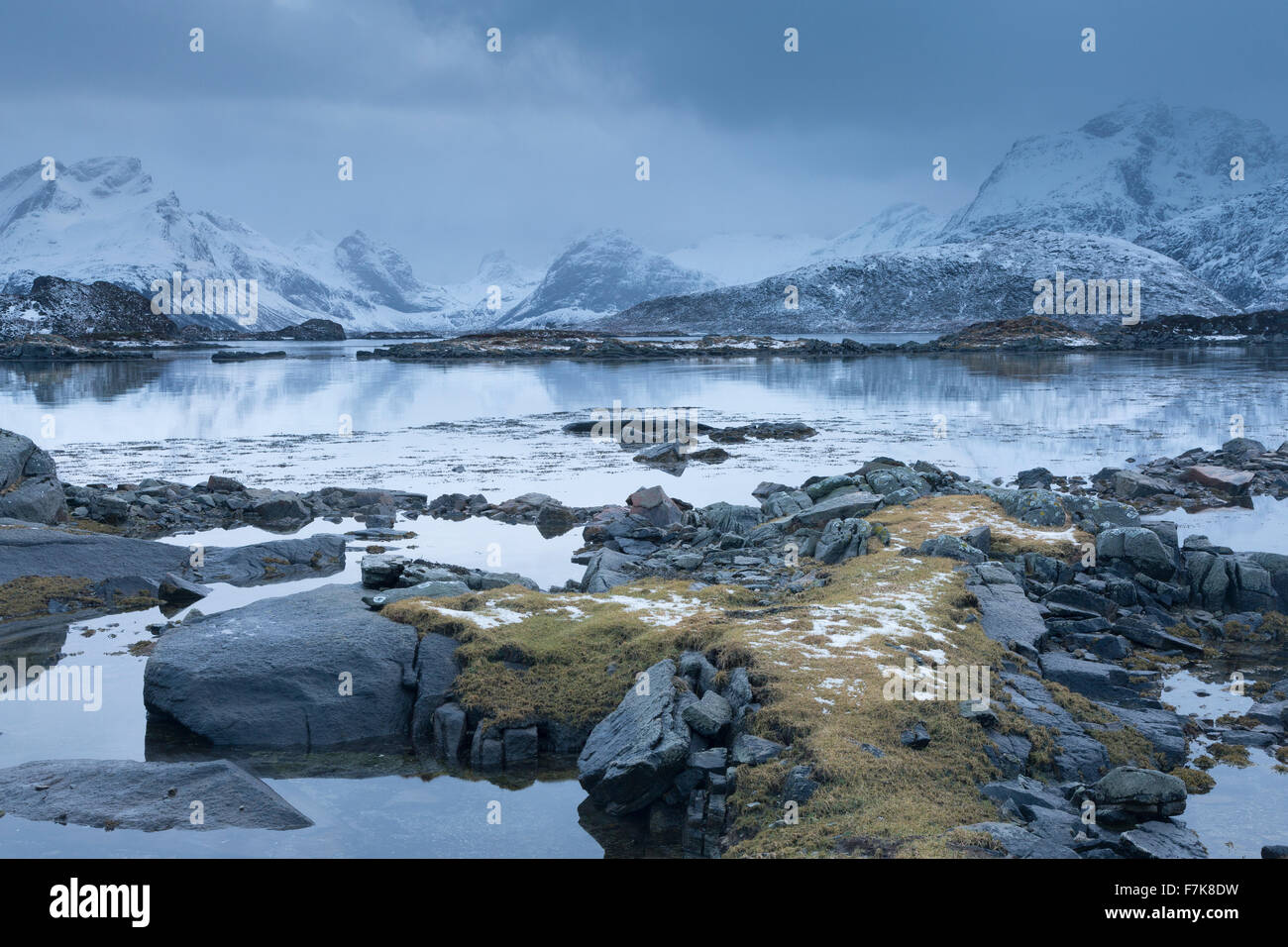 Snow covered mountains behind cold calm bay, Lofoten Islands, Norway Stock Photo