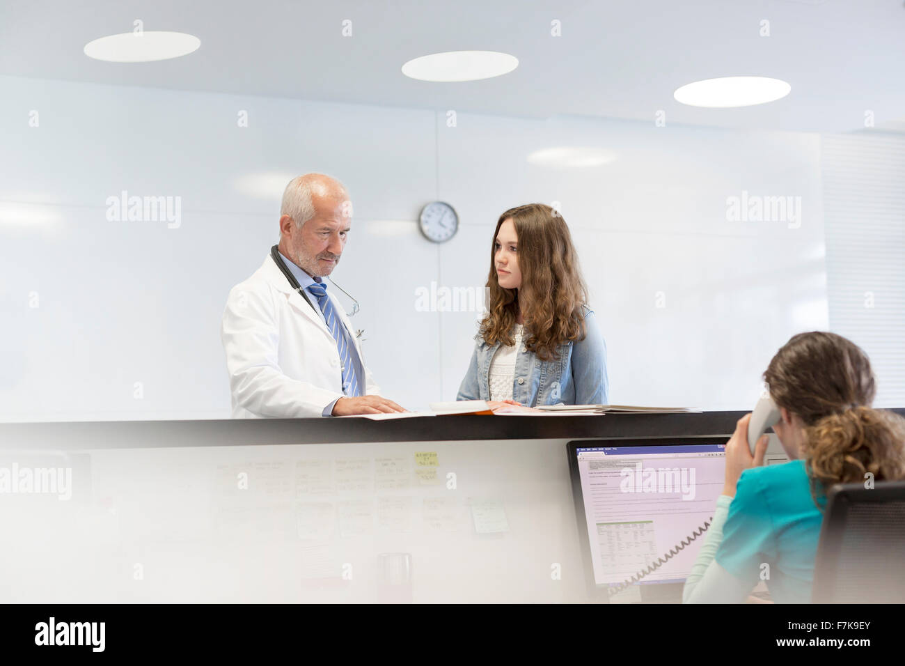 Doctor and teenage patient discussing medical record at nurses station Stock Photo
