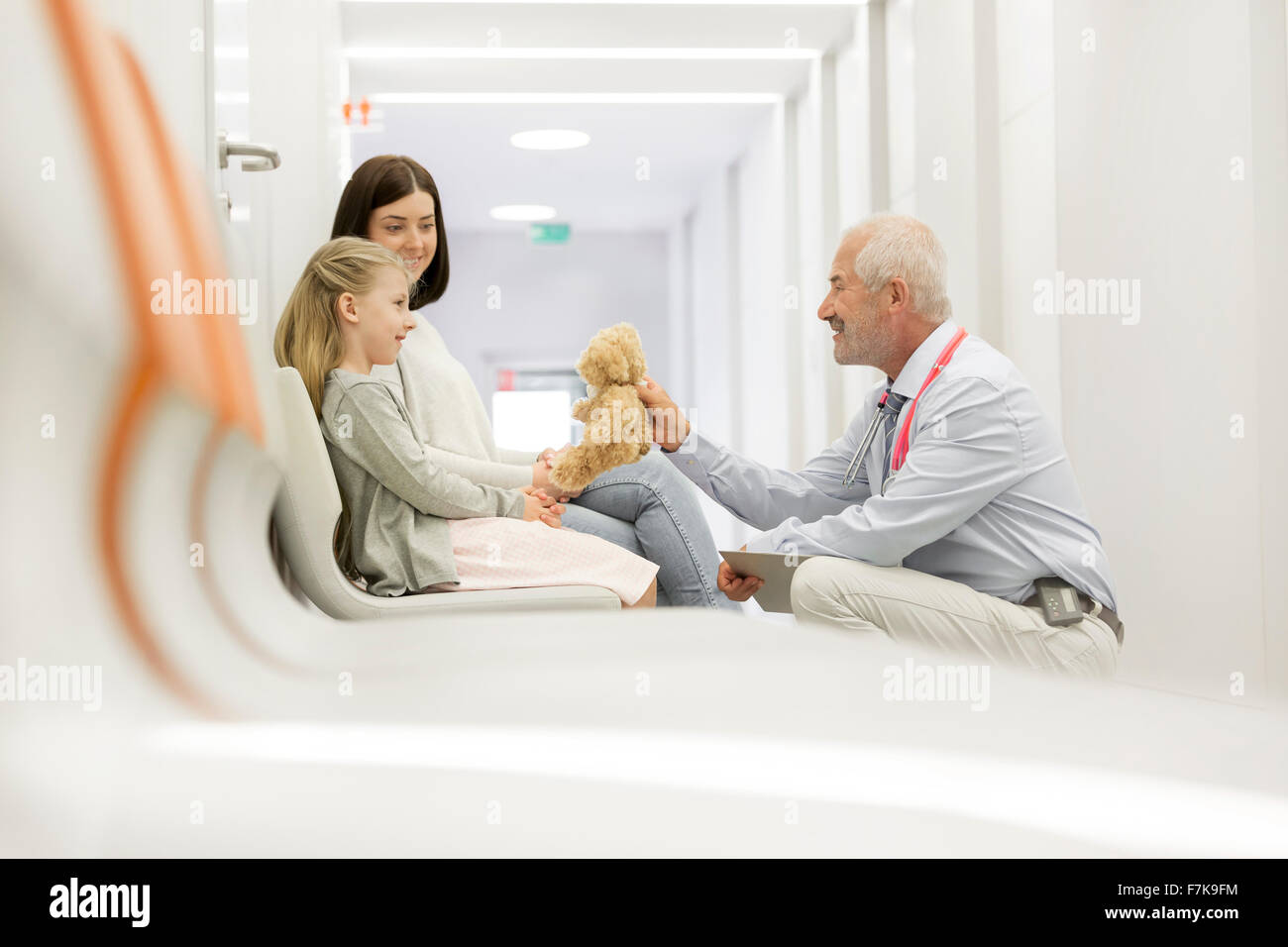 Doctor with teddy bear talking to girl patient in clinic corridor Stock Photo