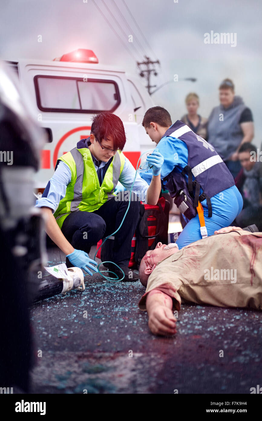 Rescue workers tending to car accident victim in road Stock Photo