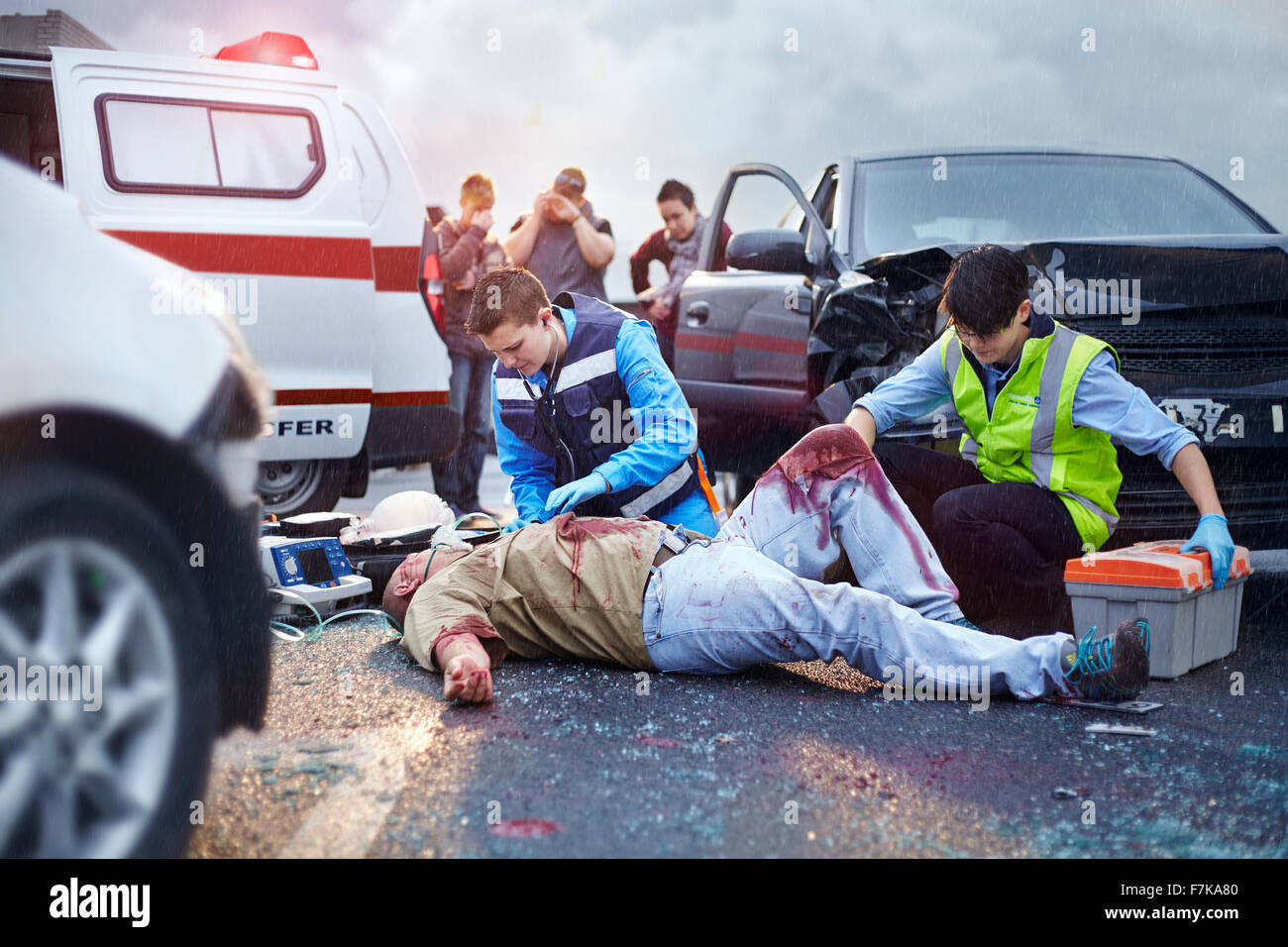 Rescue workers tending to bloody car accident victim in road Stock Photo