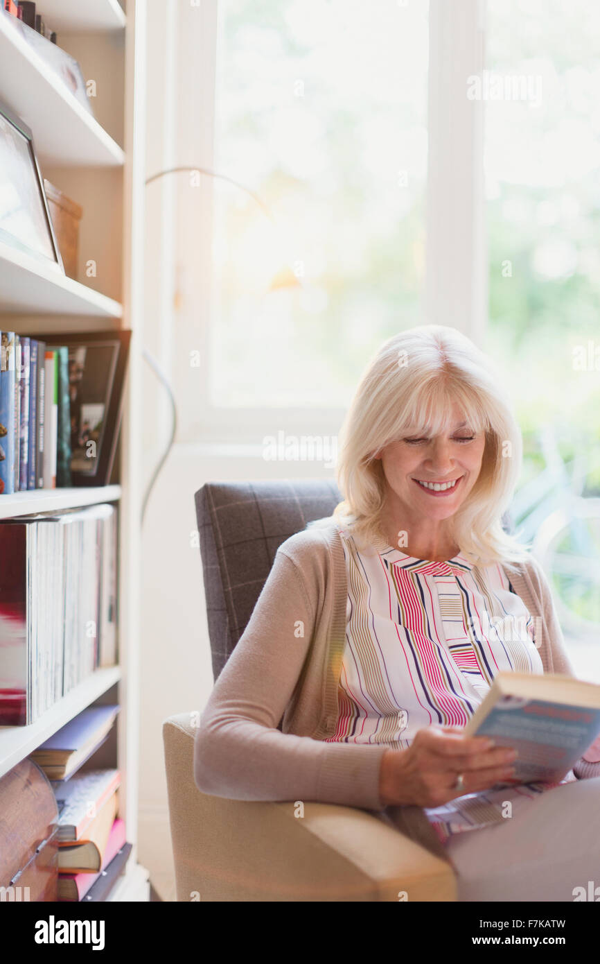 Smiling senior woman reading book in den Stock Photo
