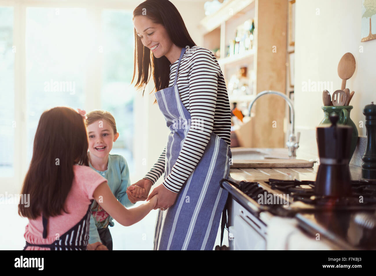 Mother and daughters holding hands in kitchen Stock Photo