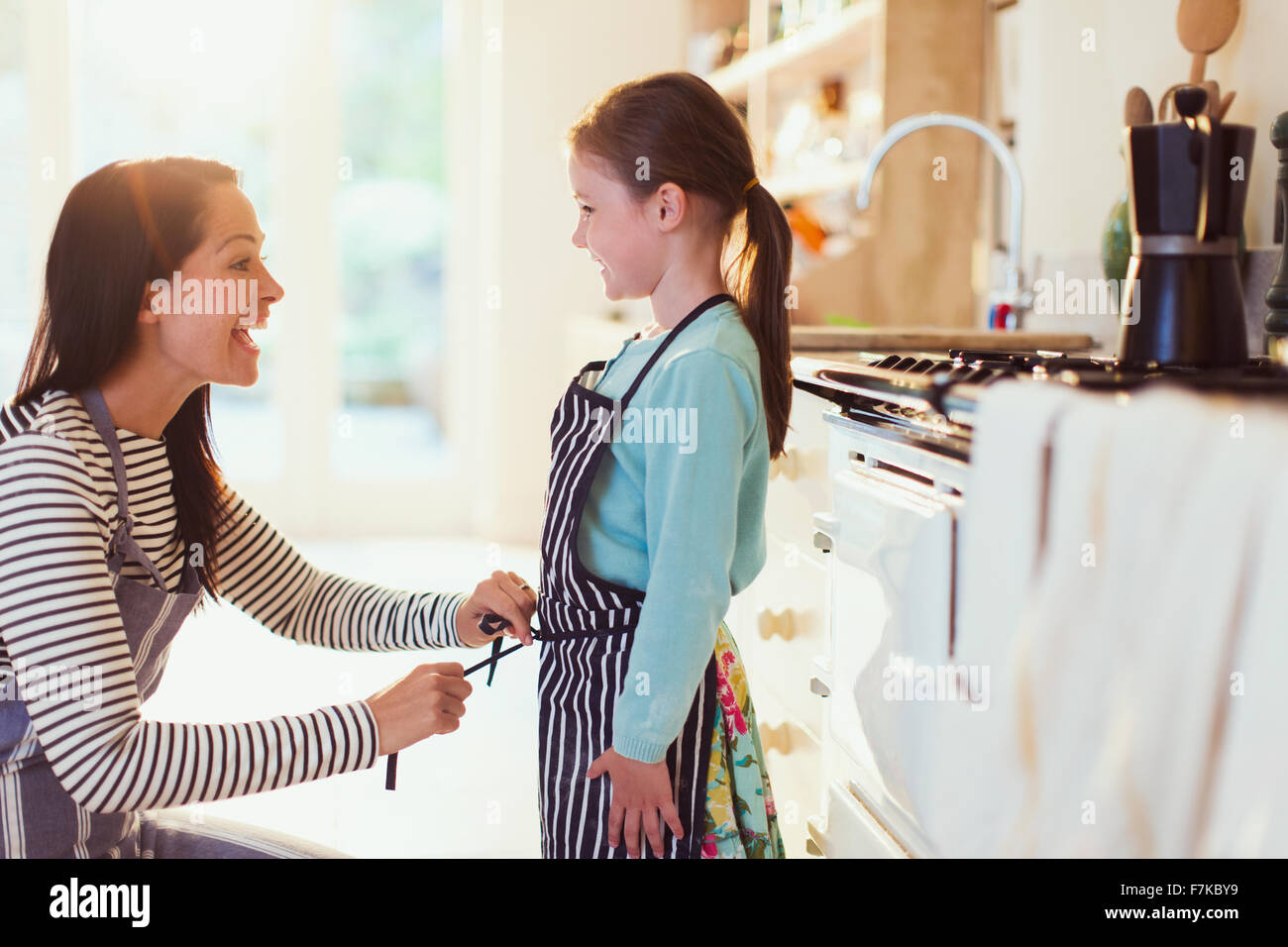 Mother tying apron on daughter in kitchen Stock Photo