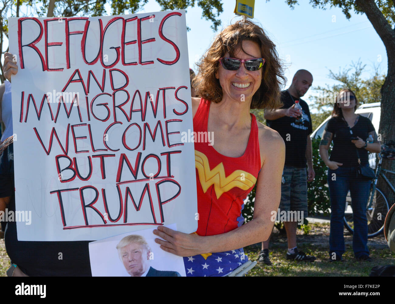 Woman in colorful Wonder woman type costume holds protest sign reading 'Refugees and immigrants welcome, but NOT TRUMP' at GOP Florida Rally Stock Photo