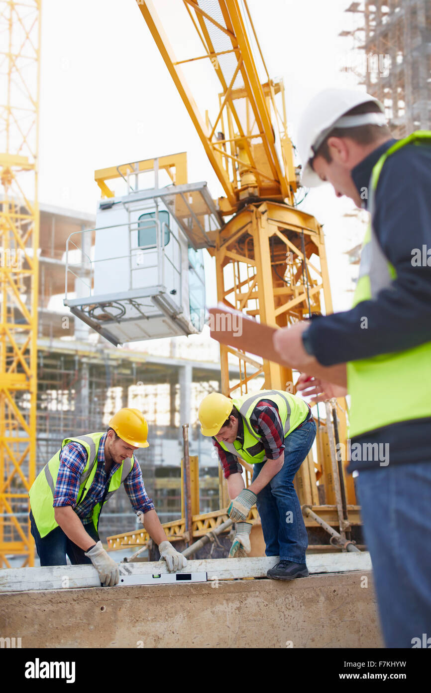 Construction workers using level tool below crane at construction site ...