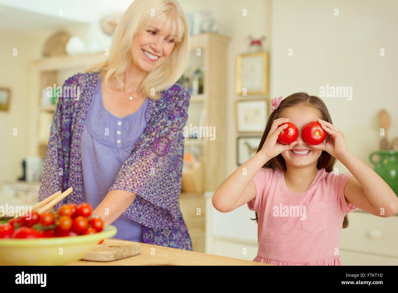 Portrait playful granddaughter covering eyes with tomatoes in kitchen Stock Photo