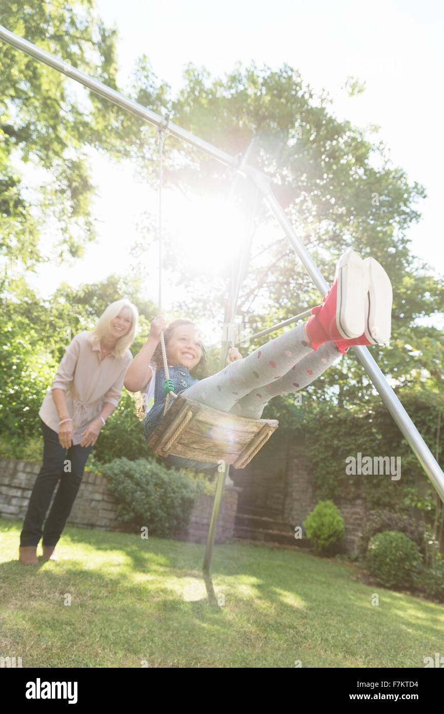 Grandmother pushing carefree granddaughter on swing in backyard Stock Photo