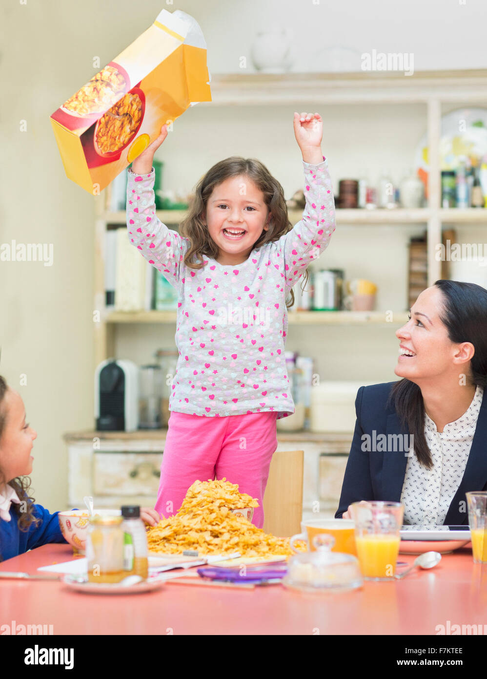Portrait enthusiastic girl cheering with cereal box at breakfast table Stock Photo