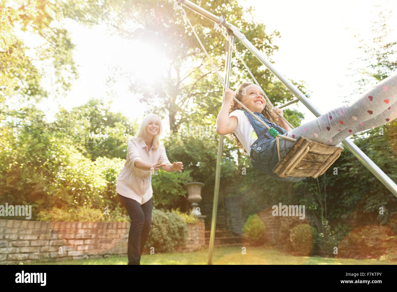 Grandmother pushing granddaughter on swing in backyard Stock Photo