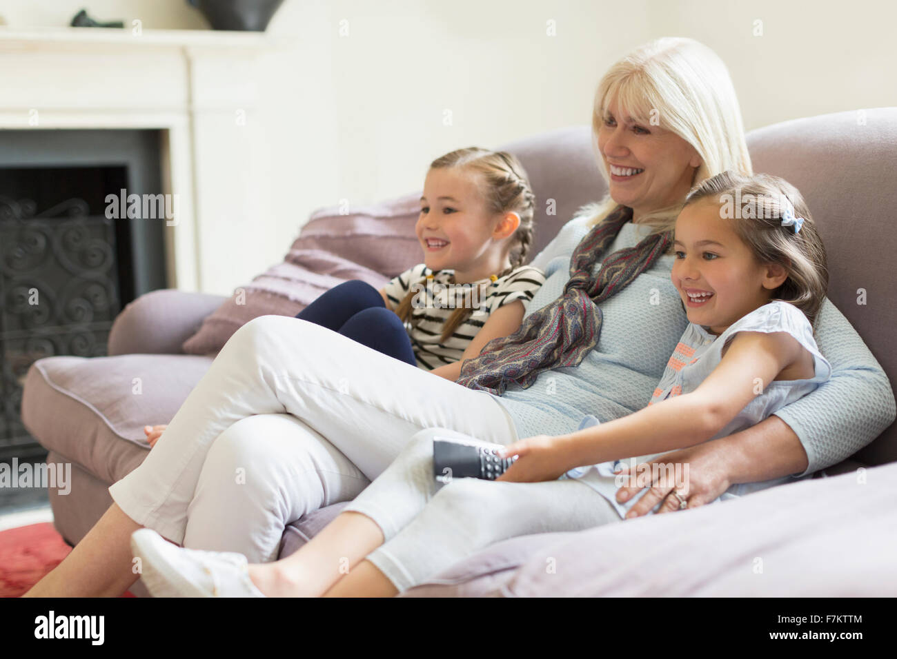 Grandmother and granddaughters watching TV on living room sofa Stock Photo