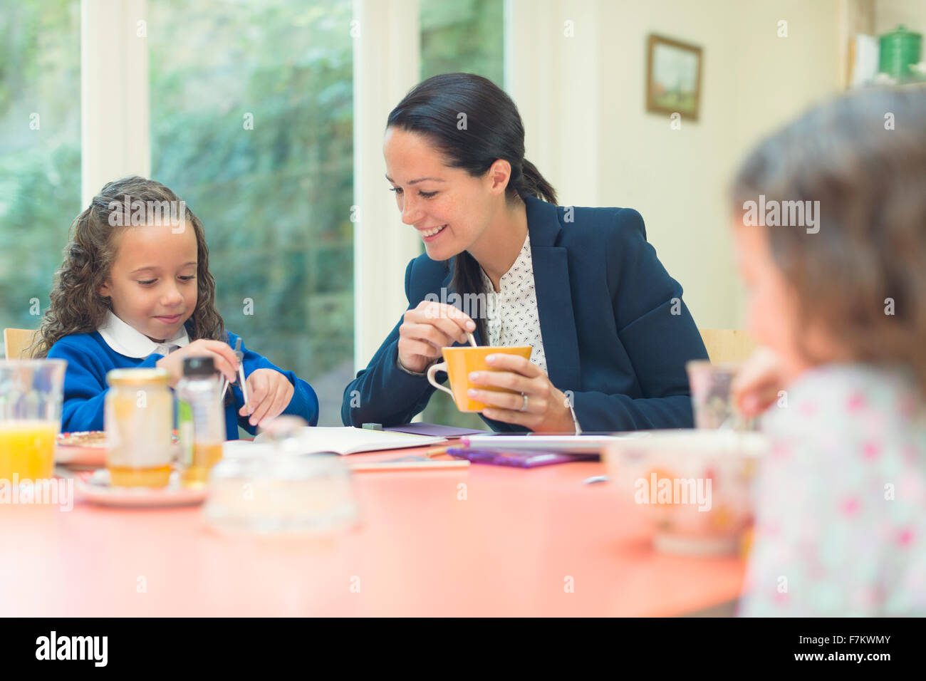 Working mother and daughter doing homework at breakfast table Stock Photo