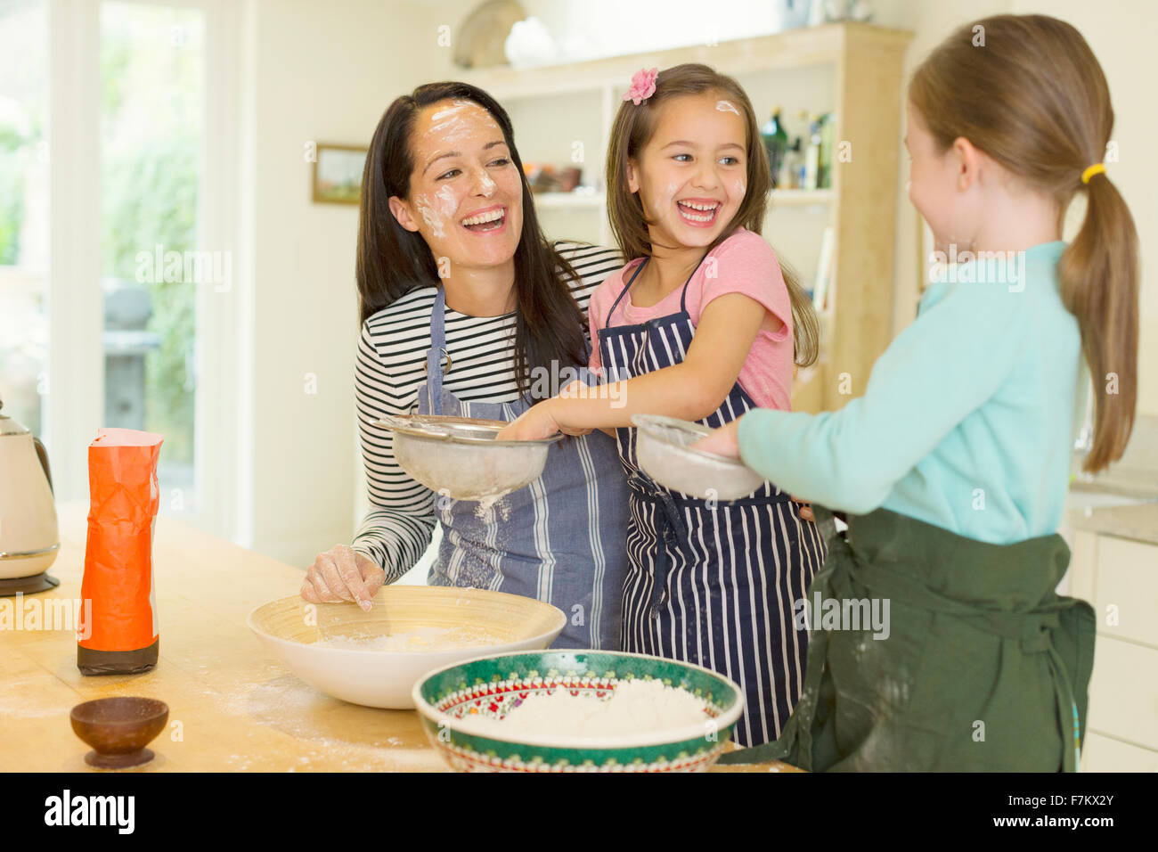 Laughing mother and daughters baking with flour on faces in kitchen Stock Photo