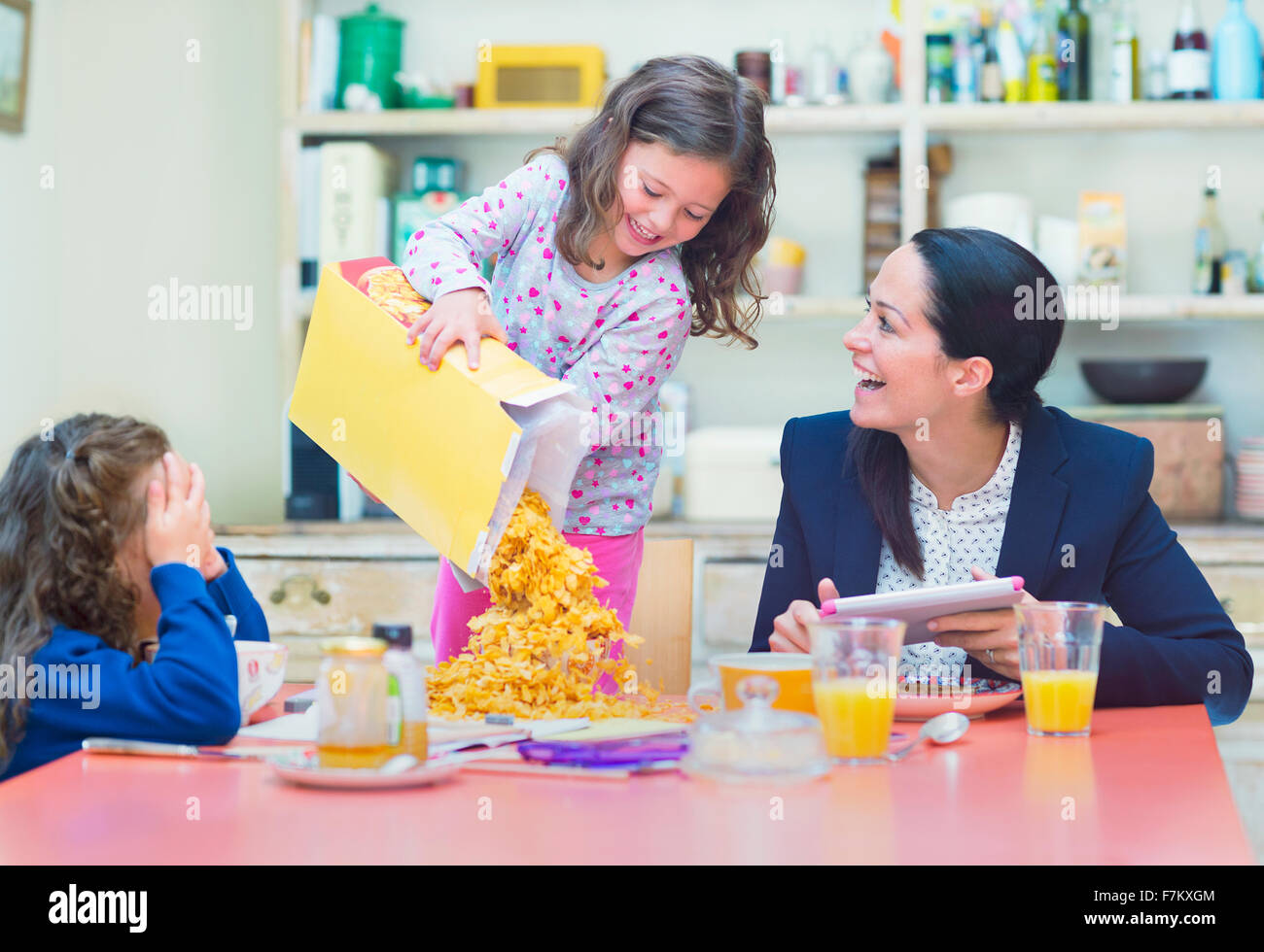 Playful girl pouring abundance of cereal onto breakfast table Stock Photo