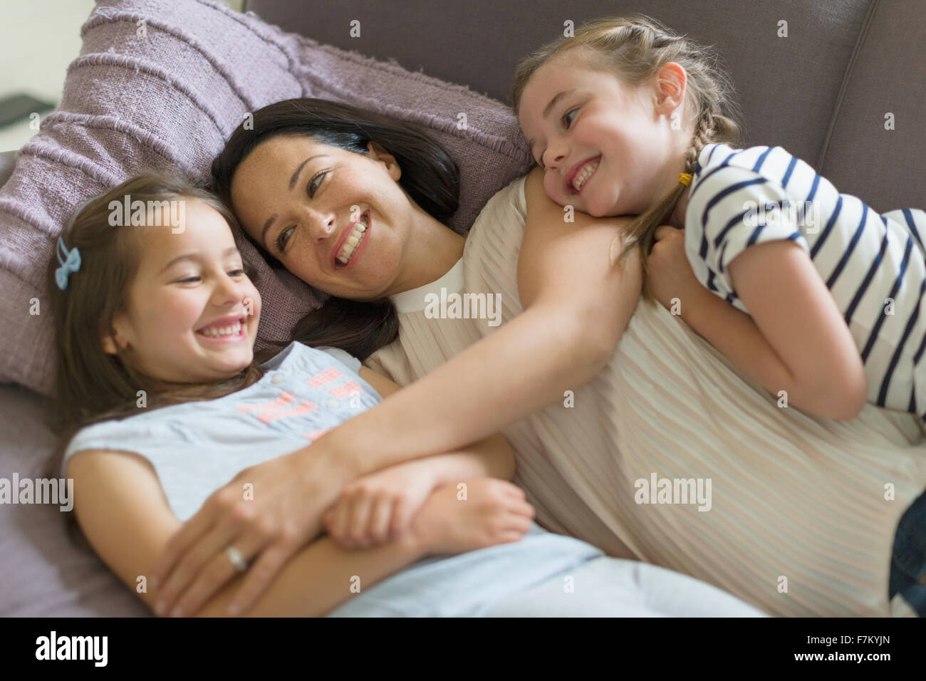 Affectionate mother and daughters cuddling on sofa Stock Photo