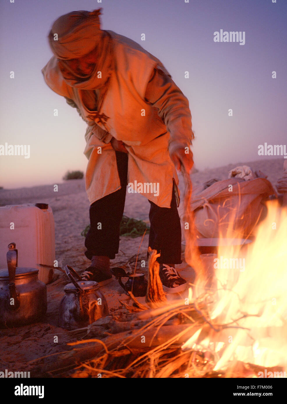 A desert guide stirs an early morning fire while on a walking trip of the Sahara. Sahara Desert, near Douz, Southern Tunisia Stock Photo