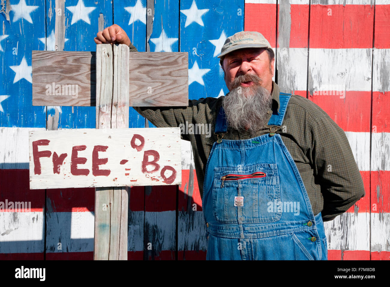 Howard the teacher poses in front of US flag and sign that says 'Free or Best Offer', near Augusta, Maine Stock Photo
