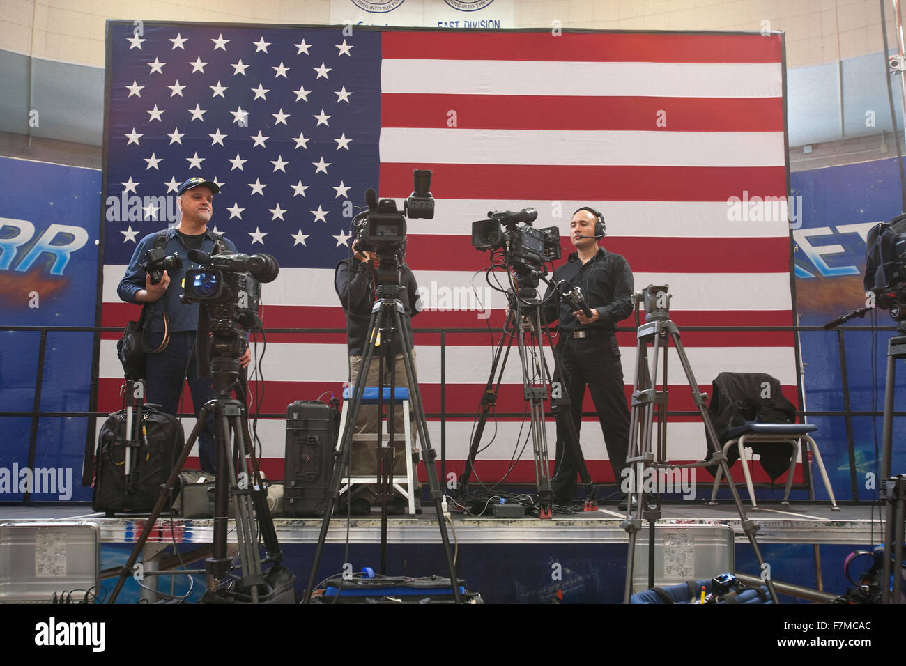 National Press and TV cameramen stand in front of a large US Flag are