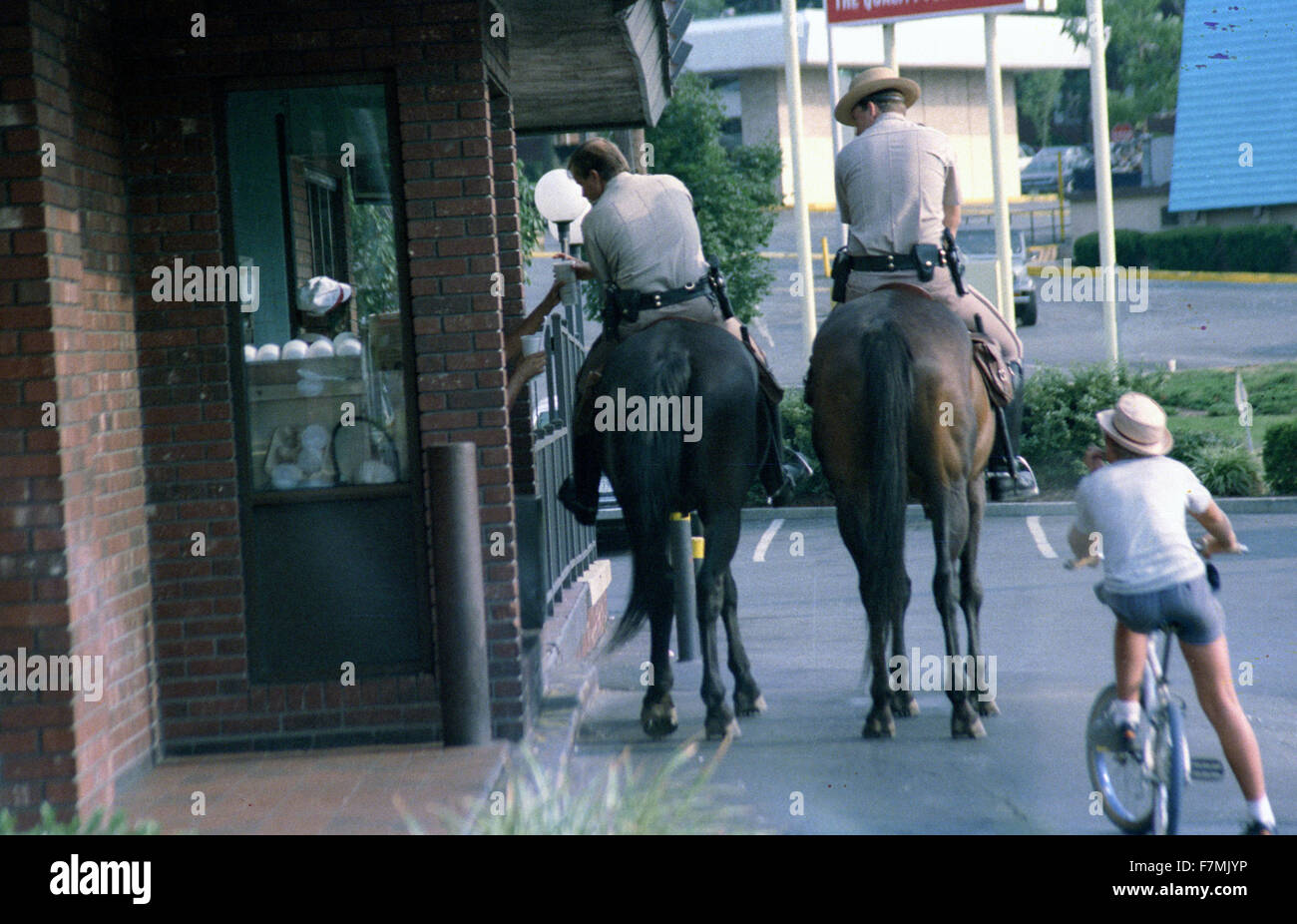 2 policemen on horseback and a small child on a bicycle at a drive in window at a McDonalds Restaurant Stock Photo