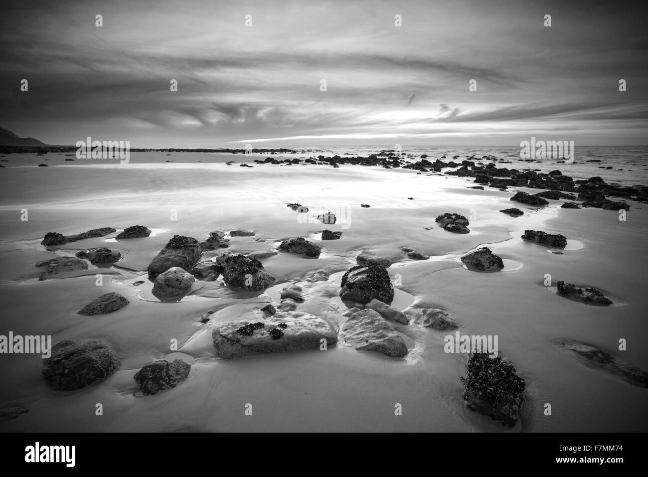 Sunrise landscape on rocky sandy beach with vibrant sky and clouds in black and white Stock Photo
