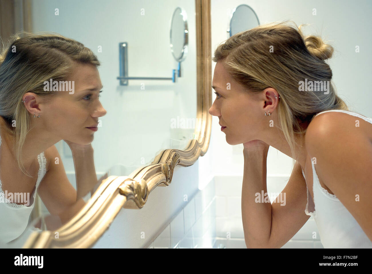 Woman looking at self in bathroom mirror Stock Photo