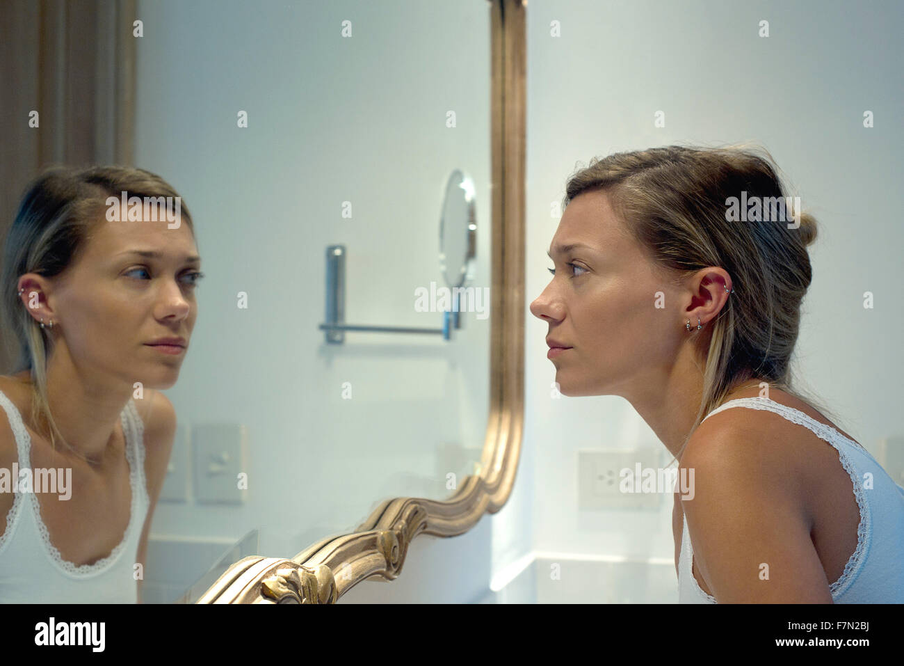 Woman looking at self in bathroom mirror Stock Photo