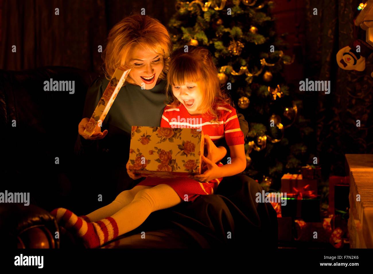 Happy mother and little daughter opening gift box by a Christmas tree in cozy living room in winter Stock Photo