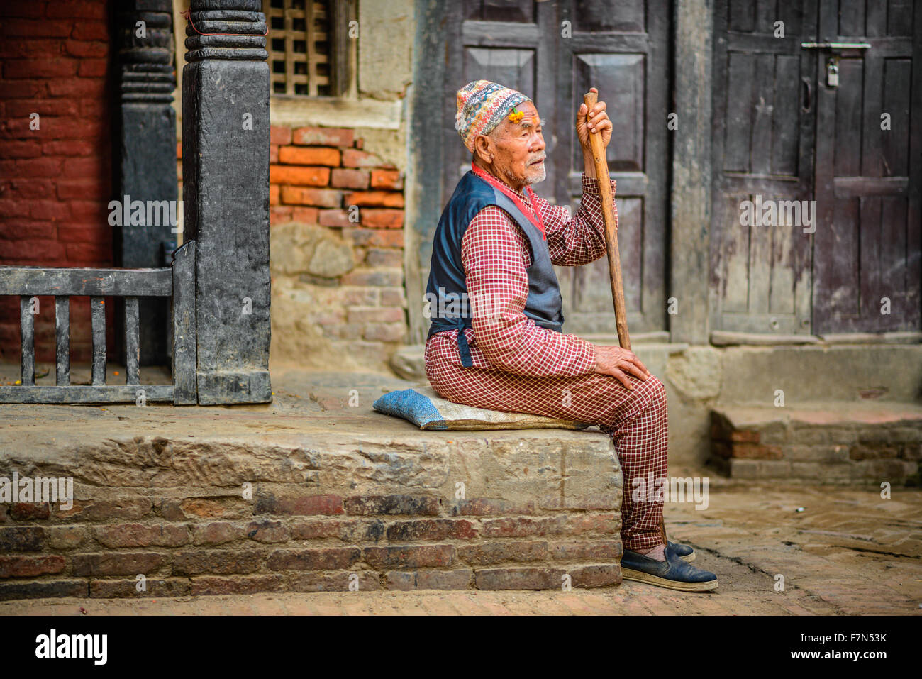 Elderly beggar with a walking stick sits in the street of Kathmandu Stock Photo