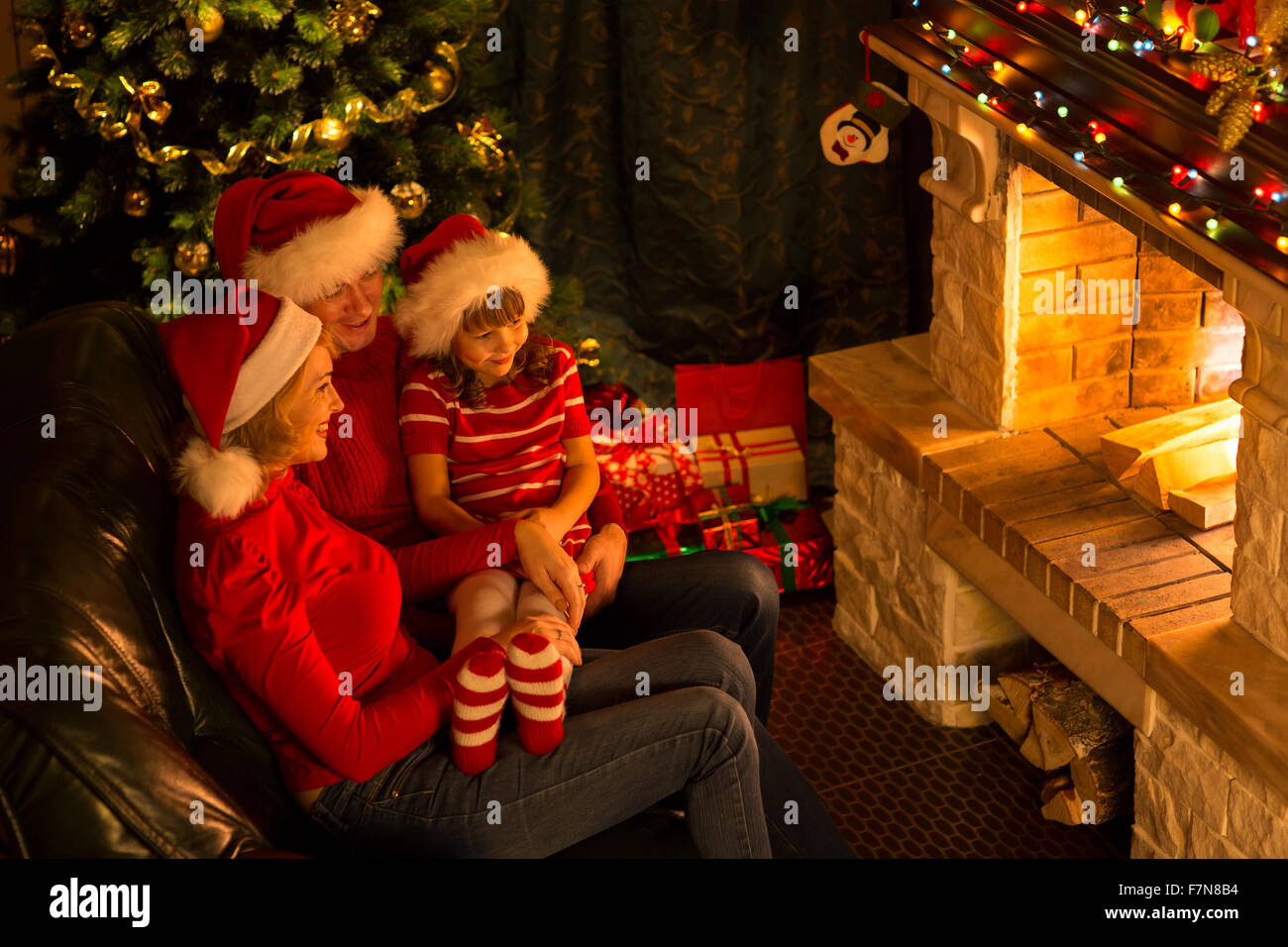 Family - mother, father and their little daughter sitting by a fireplace in a cozy dark living room on Christmas eve Stock Photo