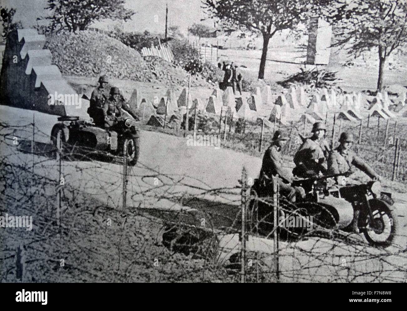 Photograph of Nazi soldiers riding motor-cycles down a barbed wired road. Dated 1943 Stock Photo