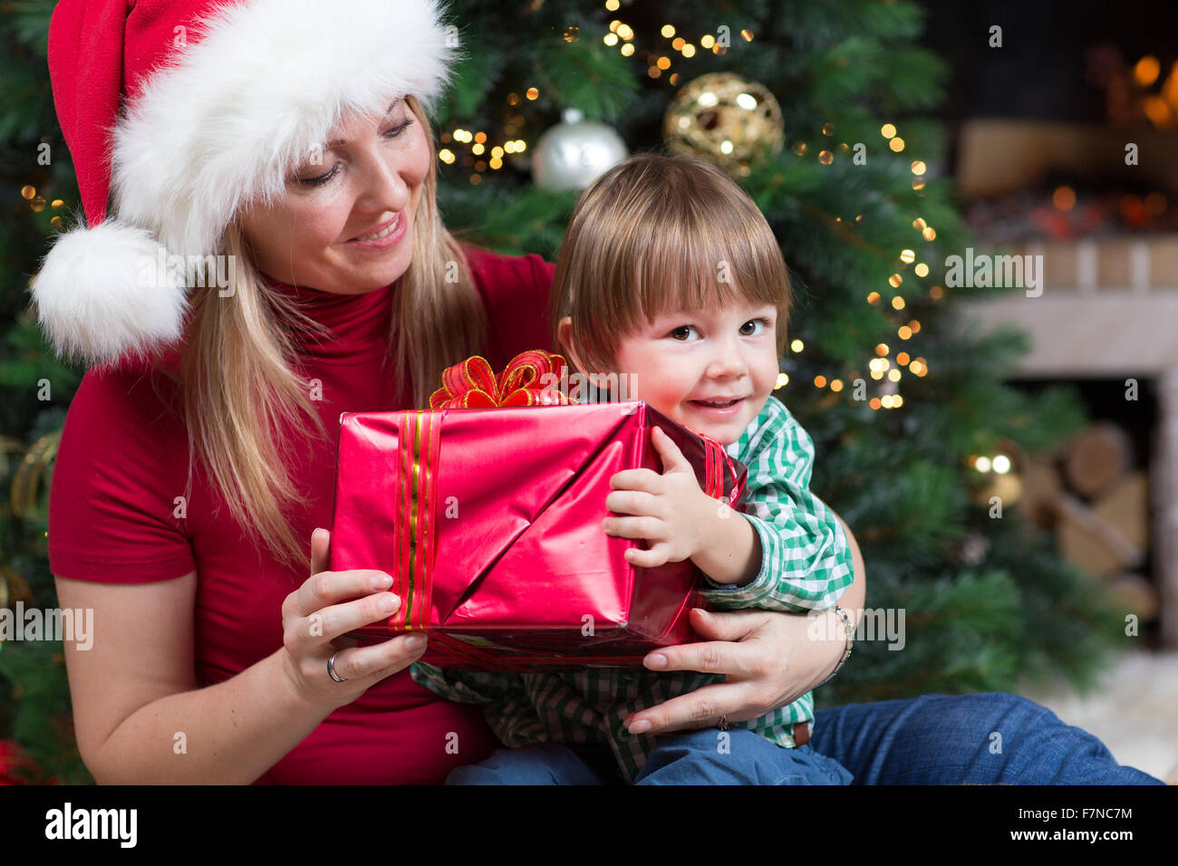 Happy woman gives wrapped christmas presents gifts to child baby toddler sitting near Christmas tree Stock Photo