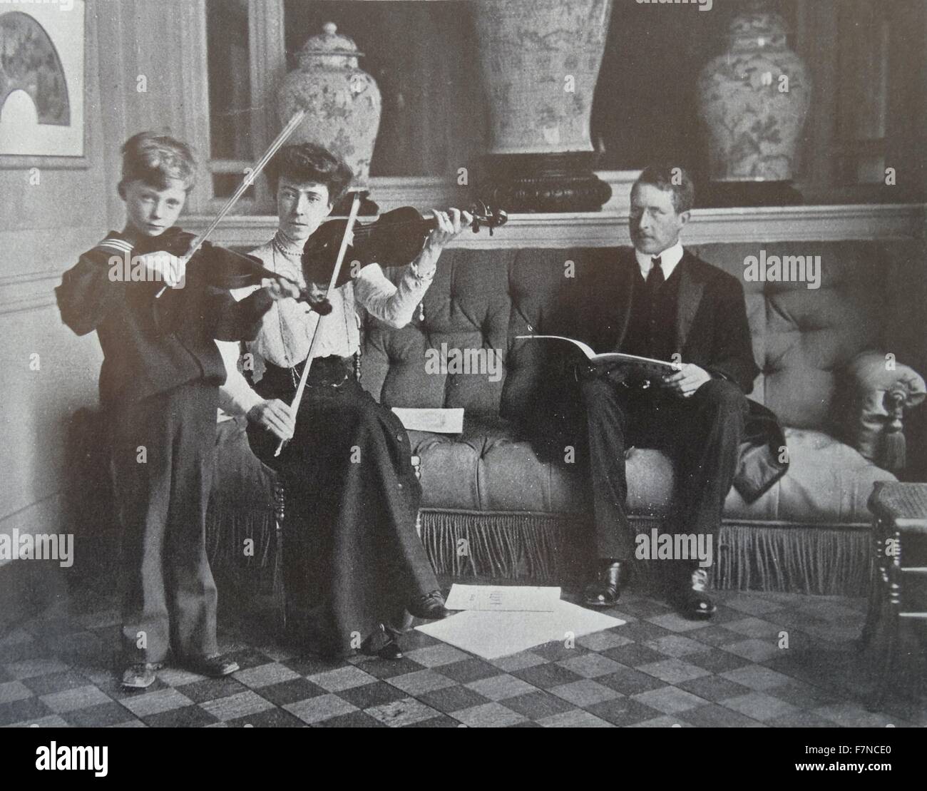 Elisabeth of Bavaria, Queen of Belgium (1876-1965) seen teaching the violin to Prince Leopold, Duke of Brabant, watched by King Albert. Stock Photo
