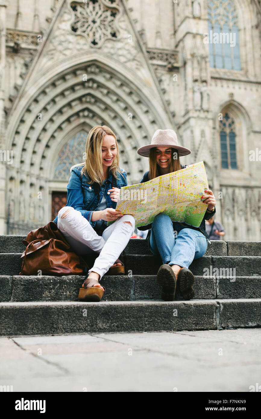Spain, Barcelona, two happy young women reading map on stairs Stock Photo