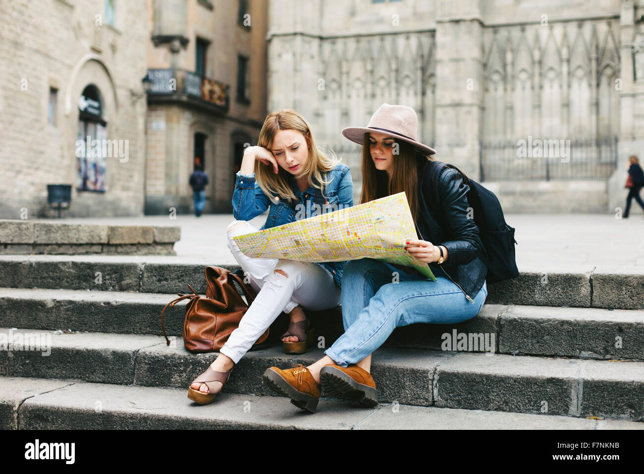 Spain, Barcelona, two young women reading map on stairs Stock Photo