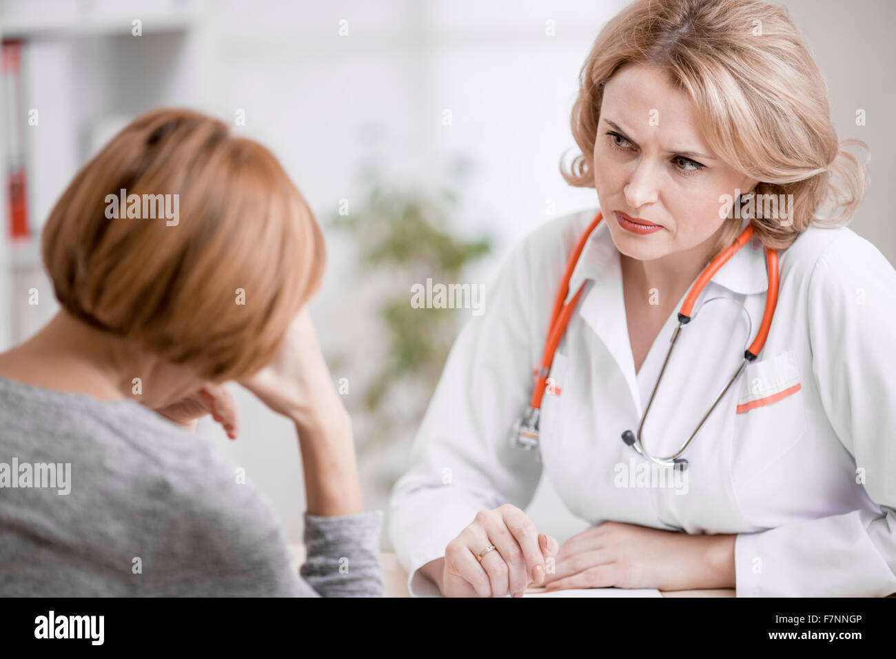 Serious doctor or physician looking at upset patient Stock Photo